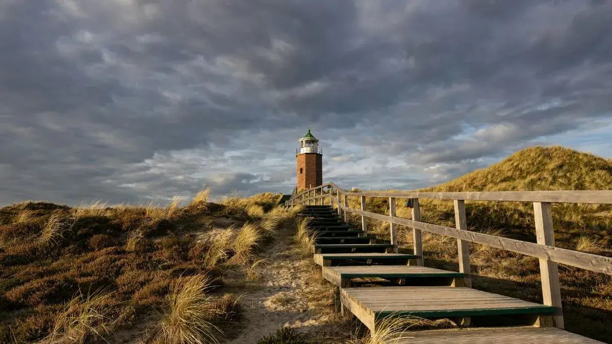 Stufen führen zu einem Leuchtturm auf Sylt mit grauen Wolken.